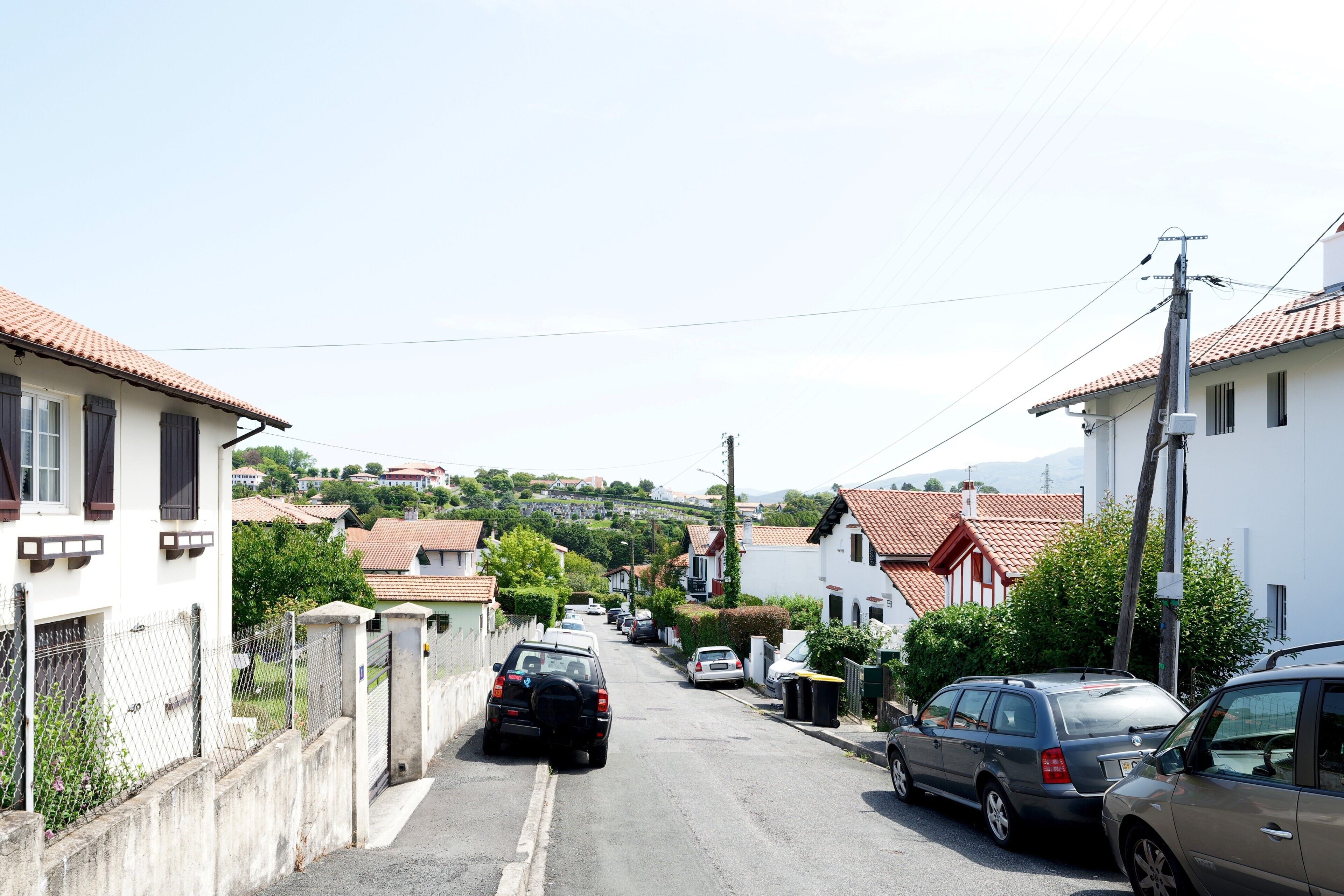 Una calle residencial con casas, coches estacionados y un paisaje montañoso al fondo.