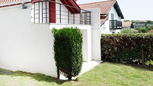 Ein weißes Gebäude mit rotem Ziegeldach, einem kleinen Balkon und einer Hecke im Vordergrund.