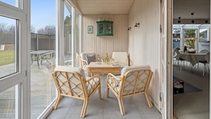 An interior space with a dining area featuring wicker chairs and a table, a green cabinet, and a view through large windows to an outdoor deck. - "Andine" - 1.2km from the sea by Interhome (Fanø)