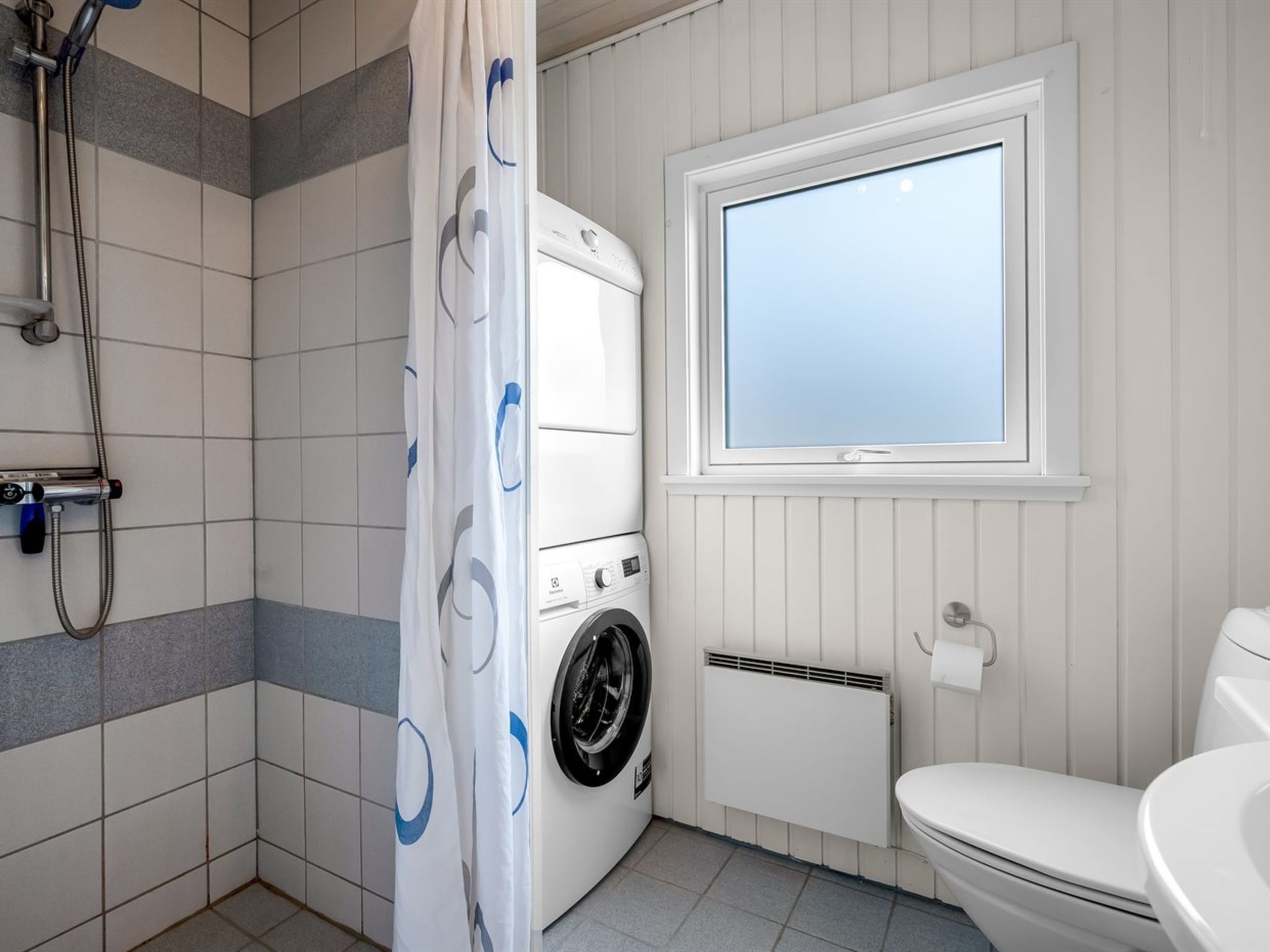 Un baño pequeño con lavadora, inodoro, ducha y ventana.