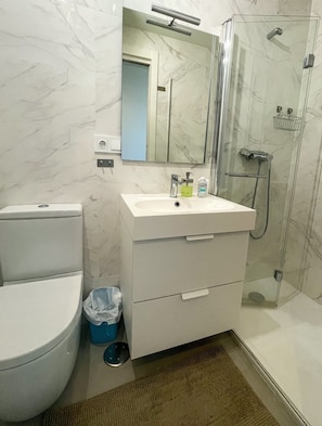 A bathroom with a toilet, sink, mirror, and shower.