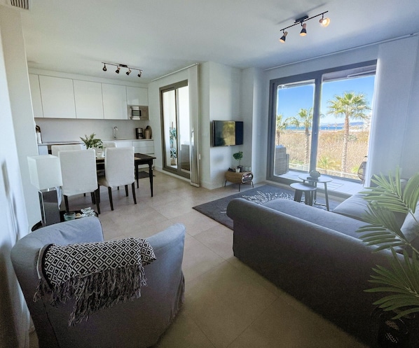 A modern living room with a sofa, a dining area with chairs, a TV, and a large window with a view.