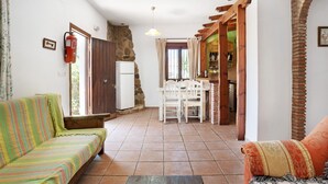 A cozy living area with a sofa, a dining table with chairs, a kitchen area, and a stone wall. - Holiday Home 'Mora' with Private Terrace, Private Garden and Wi-Fi (Vejer de la Frontera)