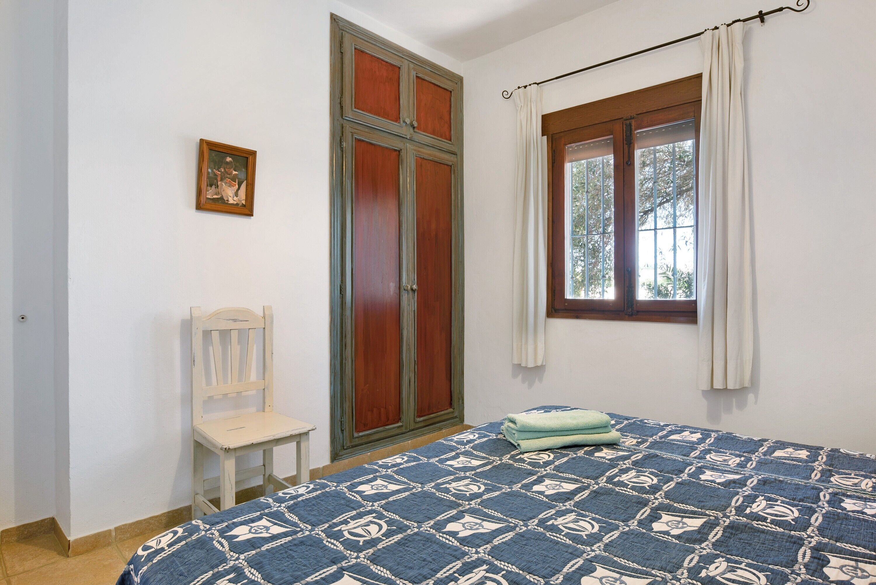 Een slaapkamer met een bed, een stoel, een kledingkast en een raam met gordijnen.