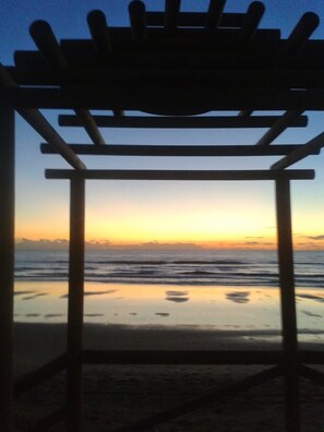 Une pergola en bois offrant une vue sur l’océan au coucher du soleil.