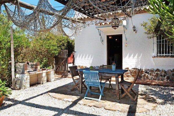 Une terrasse avec une table et des chaises, un hamac et un bâtiment blanc doté d’un toit en tuiles.