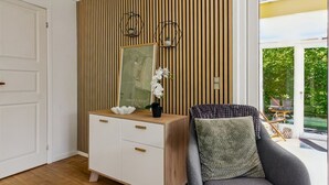A modern room with a wooden slat wall, a white cabinet with drawers, a grey armchair with a textured cushion, and a large window with a view of greenery.