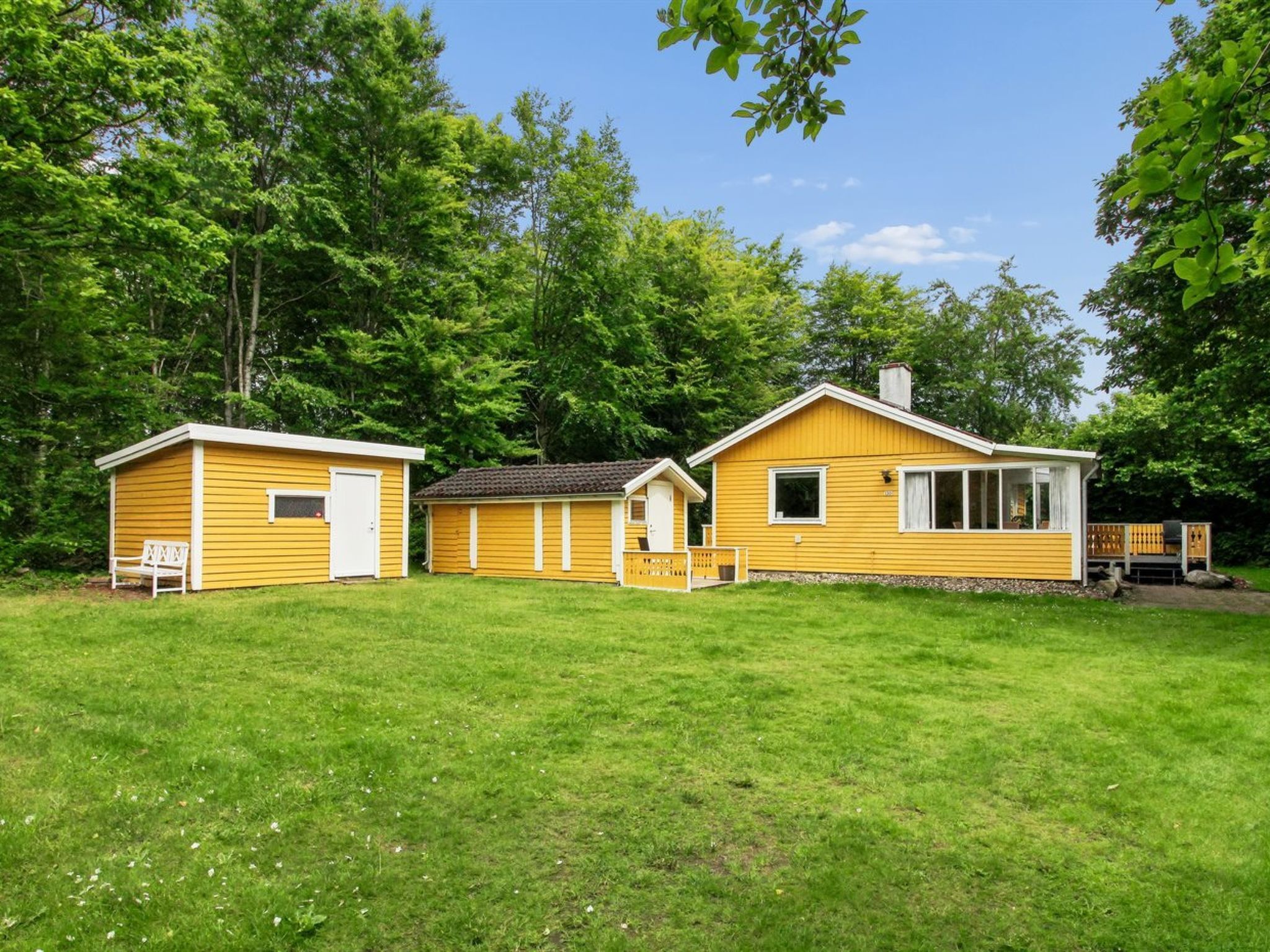 A yellow cabin with a small attached garage, surrounded by a grassy yard and trees.