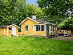 Una cabina gialla con un portico, un piccolo garage annesso e una zona salotto esterna coperta.