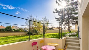 Un balcó amb taula i cadires, una escala i vista a un jardí verd amb arbres.