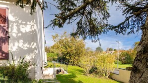 Edifici blanc amb una porta vermella, una escalinata de pedra que condueix a una zona coberta i un arbre amb fullatge verd.