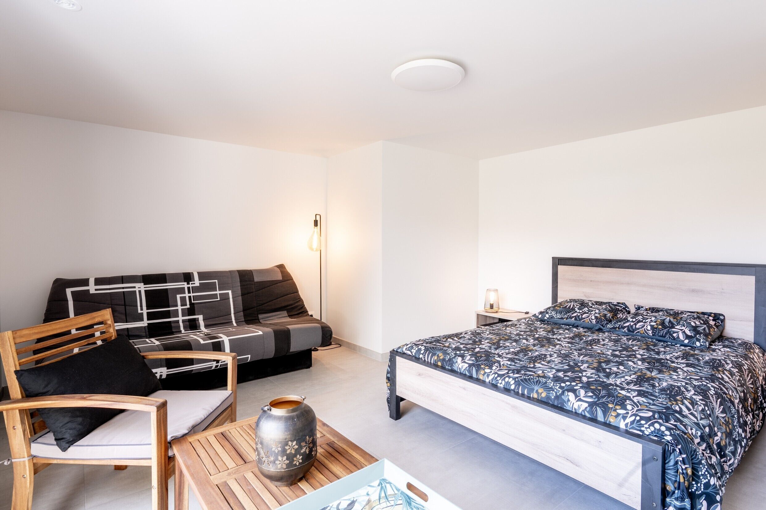 A bedroom with a bed, a sofa, a chair, a table, and a vase.