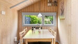 Et træinteriør med spisebord, stole, en hængende lampe, et vindue med udsigt og en informationsplakat på væggen.