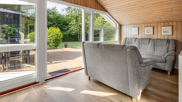 En rummelig stue med en stor skydedør til et udendørs område, en grå sofa og et træloft.