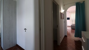 A hallway with a white door, a door frame, a light switch, and a tiled floor.