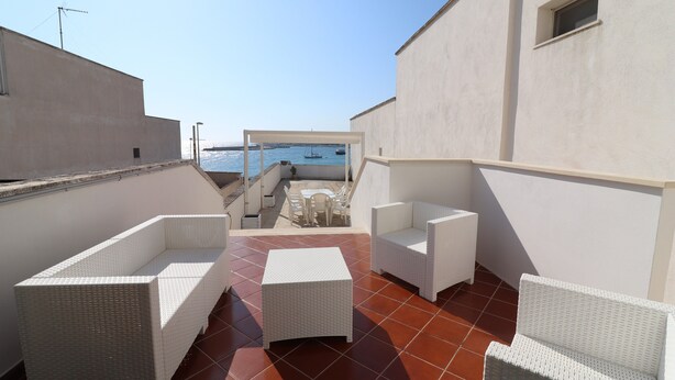 A rooftop terrace with white wicker furniture, a view of the sea, and a tiled floor.