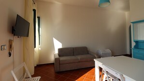 A room with a sofa, a table, a TV mounted on the wall, and a ceiling fan.