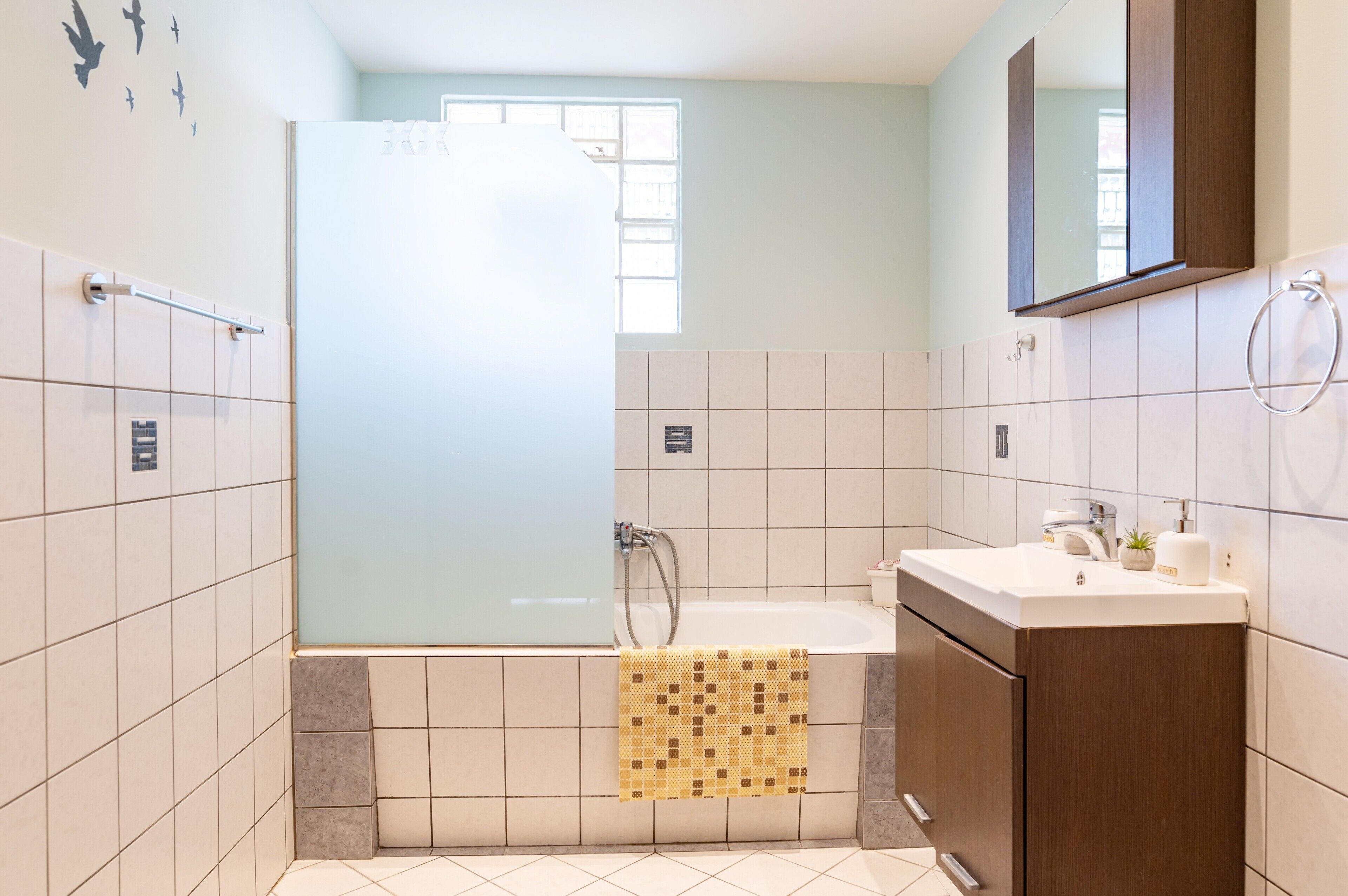 A bathroom with a glass shower enclosure, a sink with a mirror above, and tiled walls.
