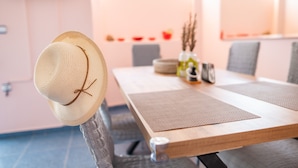 A dining table with a woven placemat, a straw hat on a chair, and a vase with branches. - Kos Dream Beachwalk Apartment with Private Terrace, Balcony, and Wi-Fi (???)