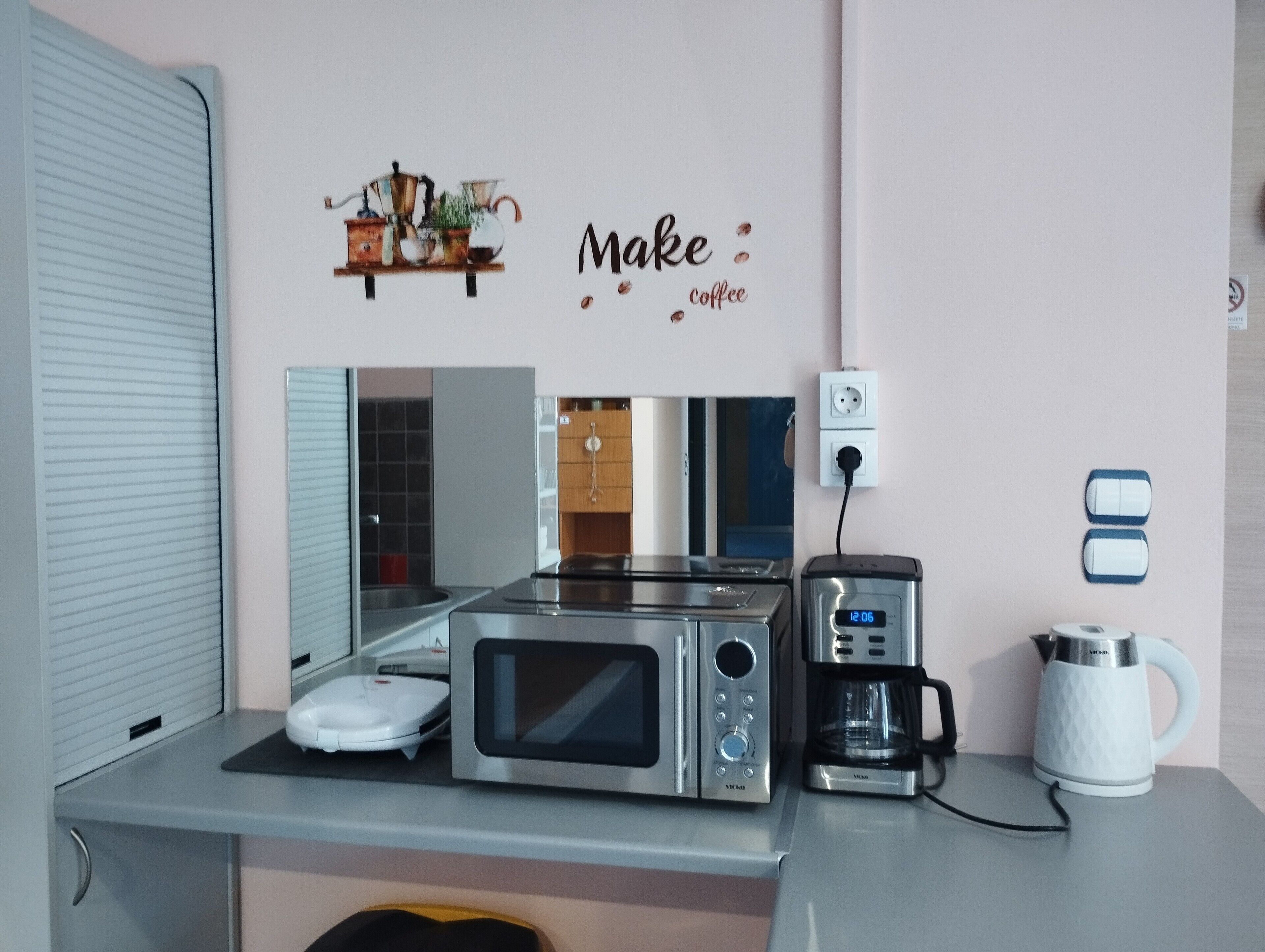 Een kitchenette met een magnetron, koffiezetapparaat en waterkoker op het aanrecht.