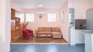 A living room with a sofa, a red chair, a coffee table, and a kitchen area with cabinets and a countertop. - Kos Dream Beachwalk Apartment with Private Terrace, Balcony, and Wi-Fi (???)