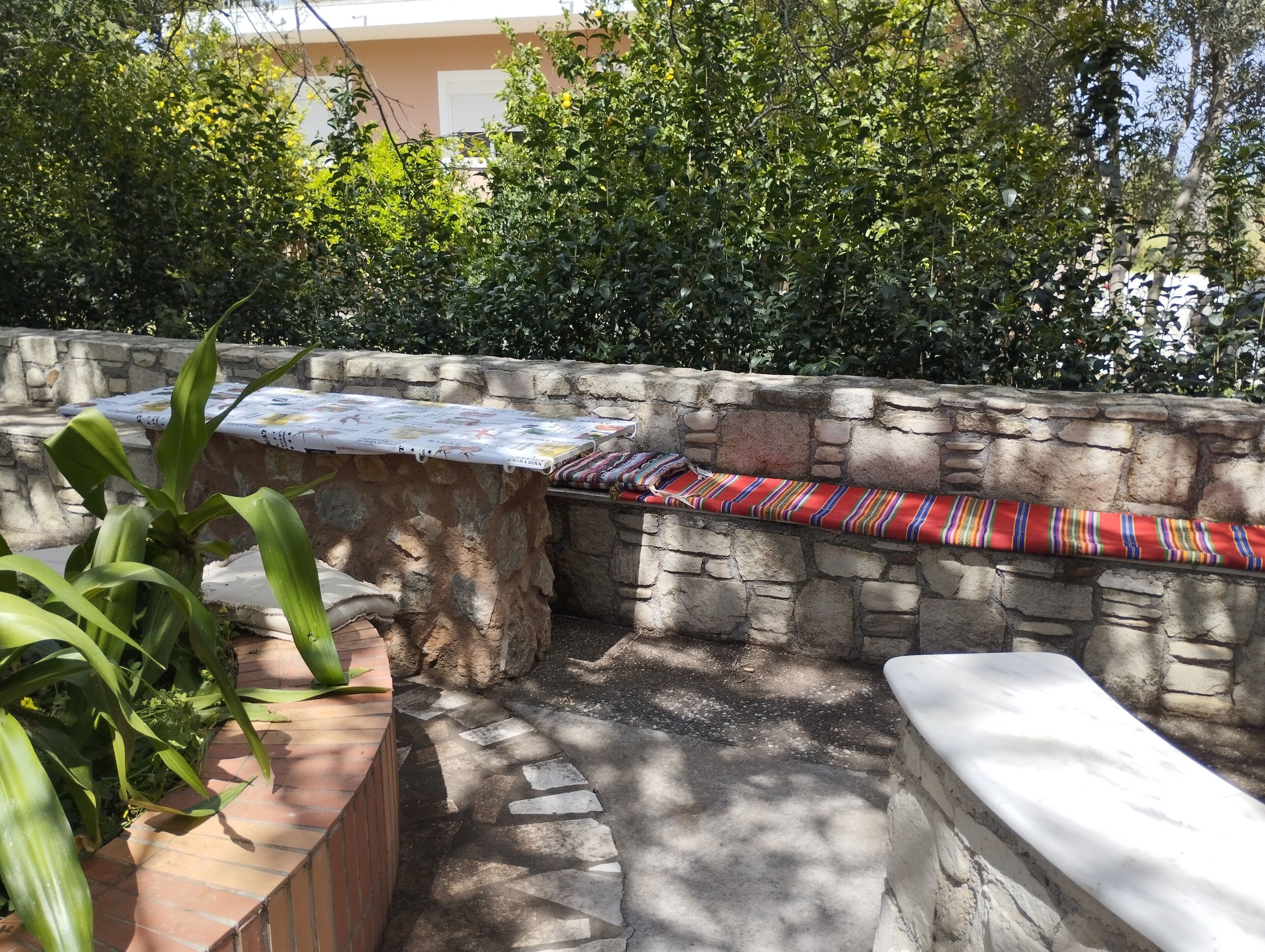 A stone wall with a bench and a table, surrounded by greenery.