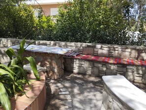 A stone wall with a bench and a table, surrounded by greenery. - Kos Dream Beachwalk Apartment with Private Terrace, Balcony, and Wi-Fi (???)