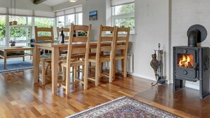 Een eetgedeelte met houten meubels, een tafel met stoelen, een vloerkleed en een houtkachel.