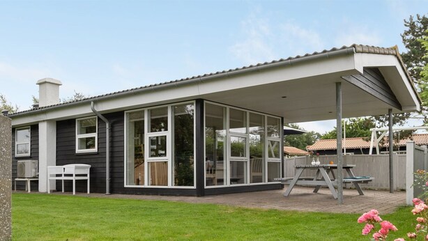 Een modern huis met een overdekt terras, een gazon en een tuin met roze bloemen.