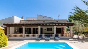 Una casa de dos pisos con piscina, mobiliario exterior y terraza cubierta.