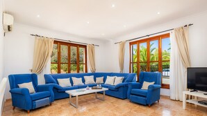 Una sala de estar con un sofá seccional azul, una mesa de centro, un televisor de pantalla plana y ventanas amplias con cortinas.