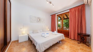 Un dormitorio con cama, mesitas de noche, una mesa, una ventana con cortinas y una obra de arte en la pared.