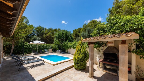 Una piscina con sillones de descanso, zona de barbacoa y una pérgola.