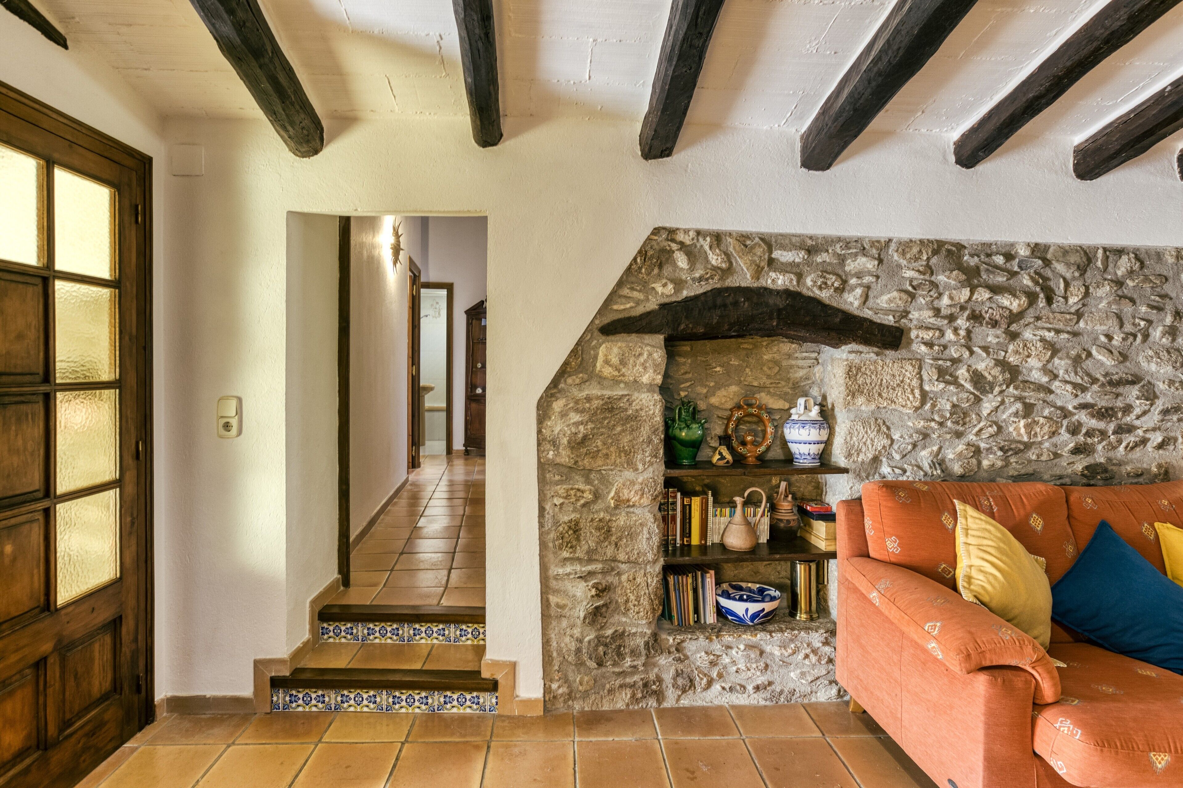 Une pièce avec un mur en pierre, une porte en bois, un escalier et un canapé avec des coussins.