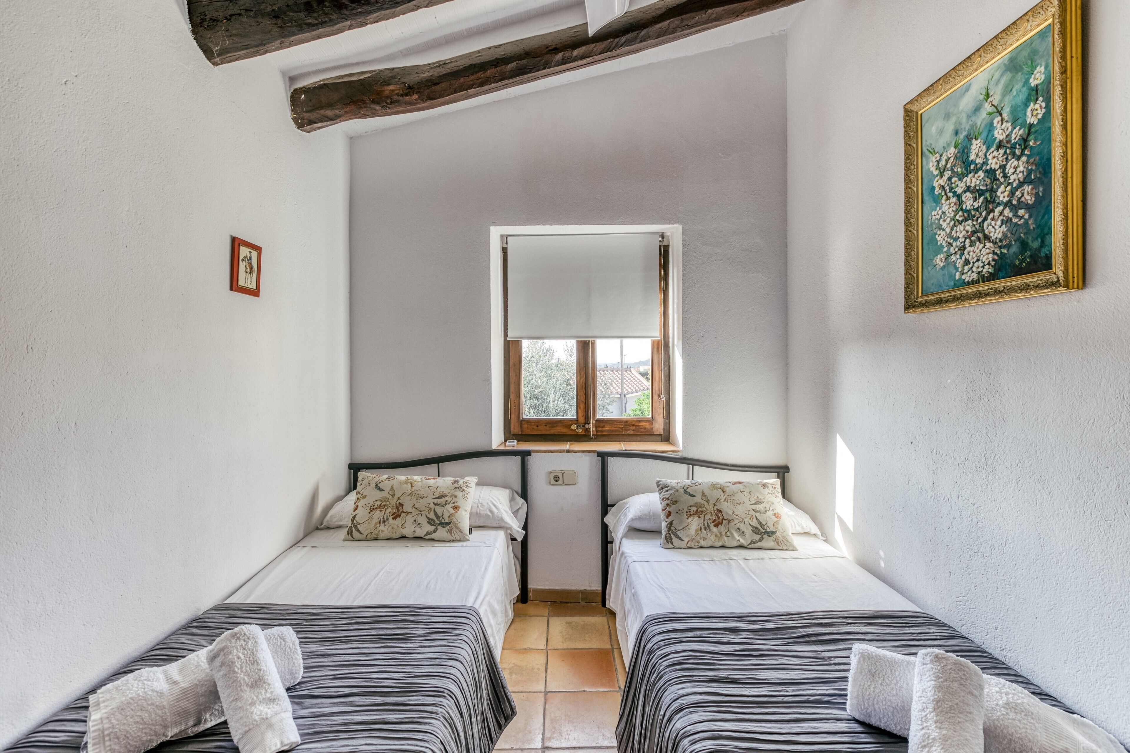 A room with two beds, a window, a painting, and a small picture on the wall.