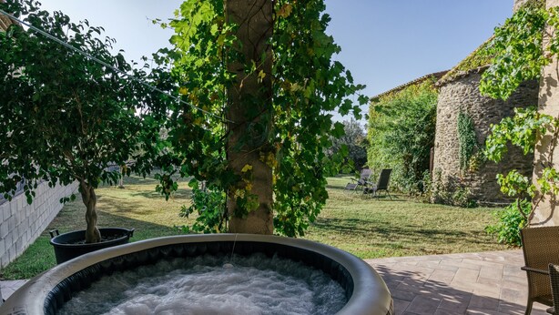 Un jacuzzi en un jardín con un muro de ladrillo, un árbol y un edificio de piedra al fondo.