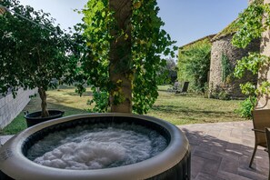 A hot tub in a garden with a brick wall, a tree, and a stone building in the background. - Vacation Home "Can Cortada" with Mountain View, Private Terrace & Barbecue (Cantallops)