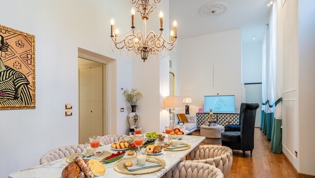 A dining area with a marble table, upholstered chairs, a chandelier, and a television in the background. - Holiday Home 'Mirò' with Private Garden, Wi-Fi & Air Conditioning (NO ZTL) (Lucca)