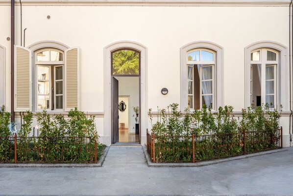 Un bâtiment doté de trois fenêtres en arc de cercle, d’une porte centrale et d’un petit jardin clos.