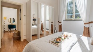 A bedroom with a bed, a bedside table, a mirror, a window with curtains, and a view of the outside. - Holiday Home 'Mirò' with Private Garden, Wi-Fi & Air Conditioning (NO ZTL) (Lucca)