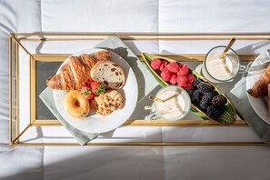 A breakfast tray with croissants, a donut, berries, and a glass of milk on a bed.