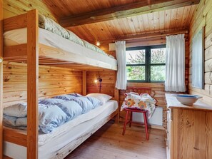 Een blokhutinterieur met een stapelbed, een bureau met stoel, en een raam met gordijnen.