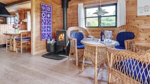 Un intérieur de chalet chaleureux, avec un revêtement mural en bois, une cheminée, des meubles en osier et un coin repas.