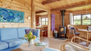 L’intérieur d’un chalet chaleureux, avec un canapé bleu, une table ronde en bois, une chaise en osier, un tapis blanc et moelleux, et un poêle à bois.