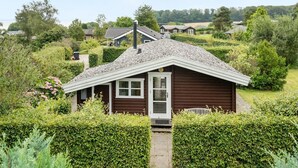 Une maison de plain-pied avec un toit en pente, entourée de haies bien entretenues et de différents types d’arbres.