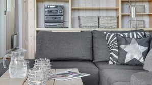 Un salon chaleureux avec une table basse en bois, un canapé gris et une bibliothèque contenant du matériel audio.
