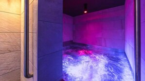 A steam room with a tiled floor and walls, a visible steam vent, and a door with a handle.