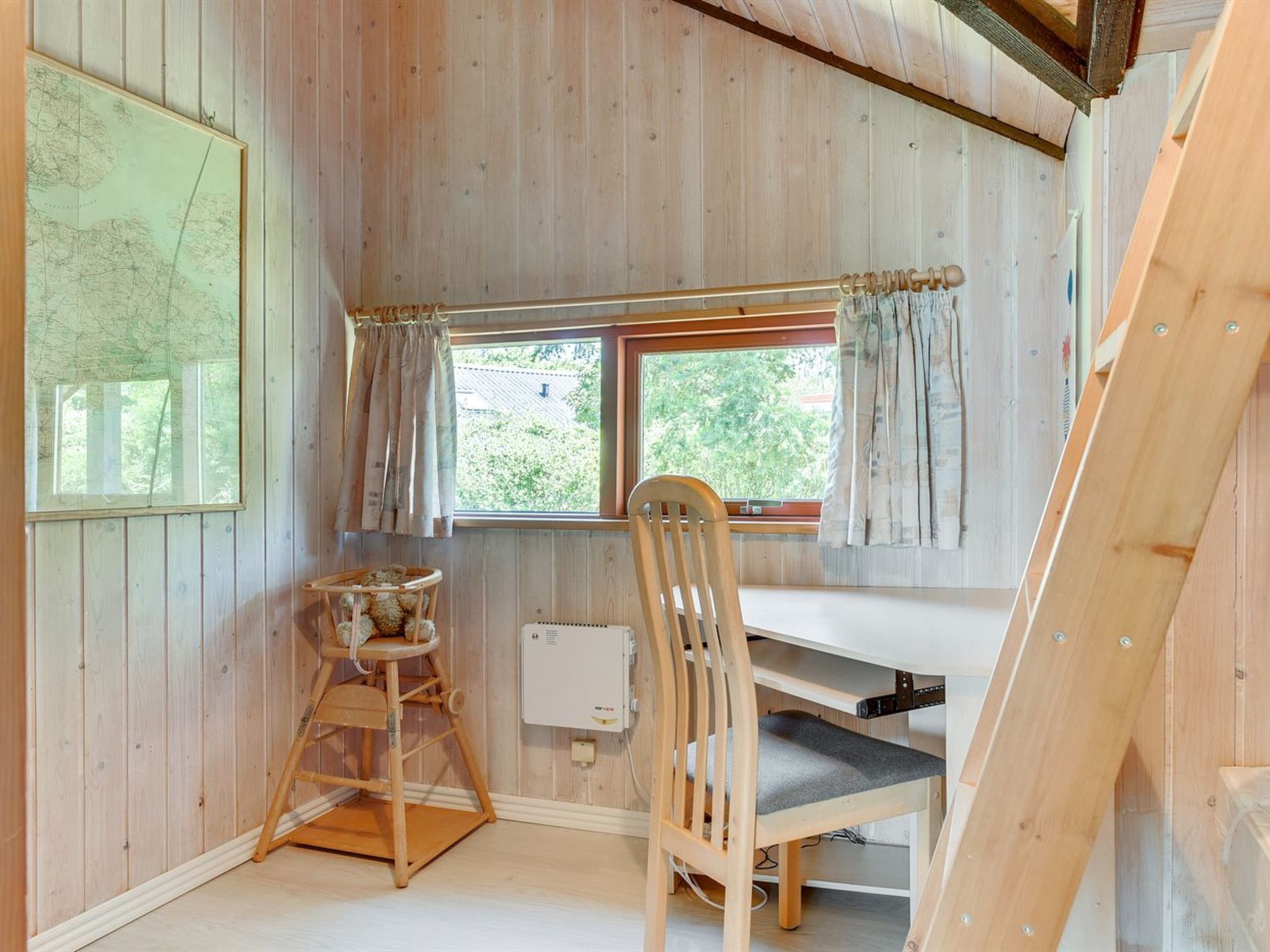 A small, wooden room with a desk, chair, and a window with curtains.