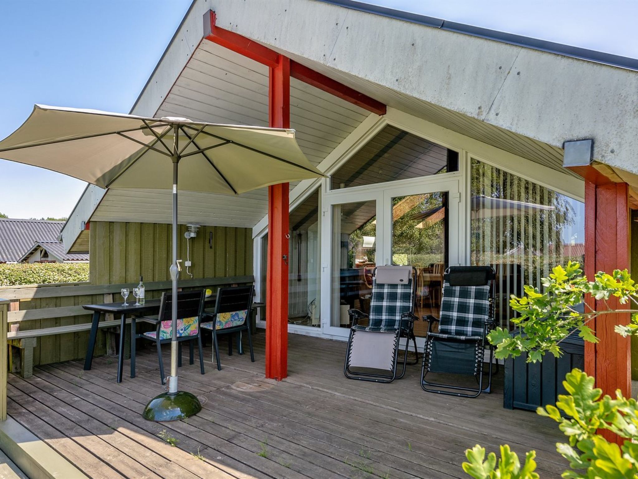 An outdoor patio with a wooden deck, a covered seating area with a table and chairs, and a large umbrella providing shade.