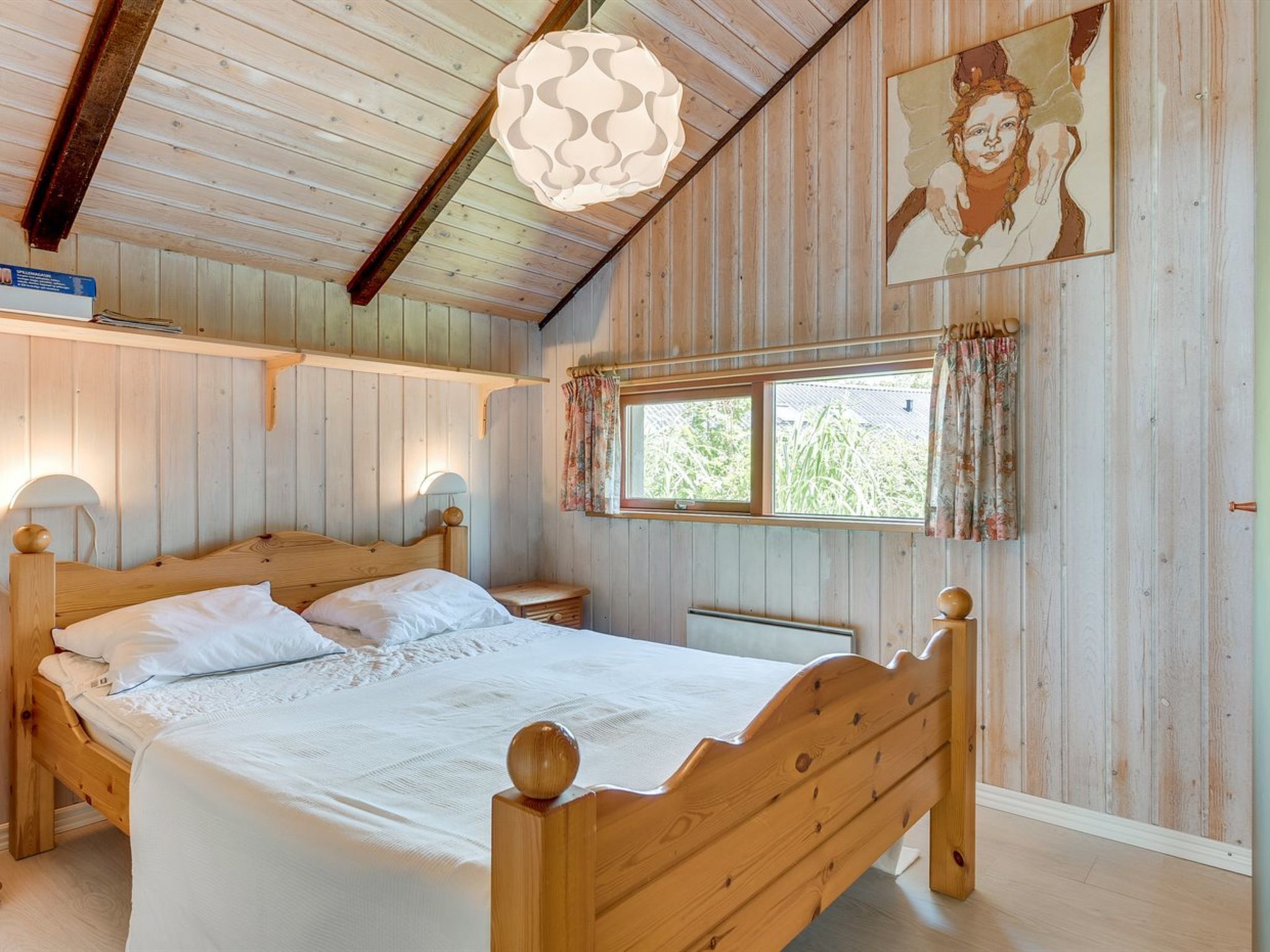 A wooden room with a bed, a window with curtains, and a hanging light fixture.